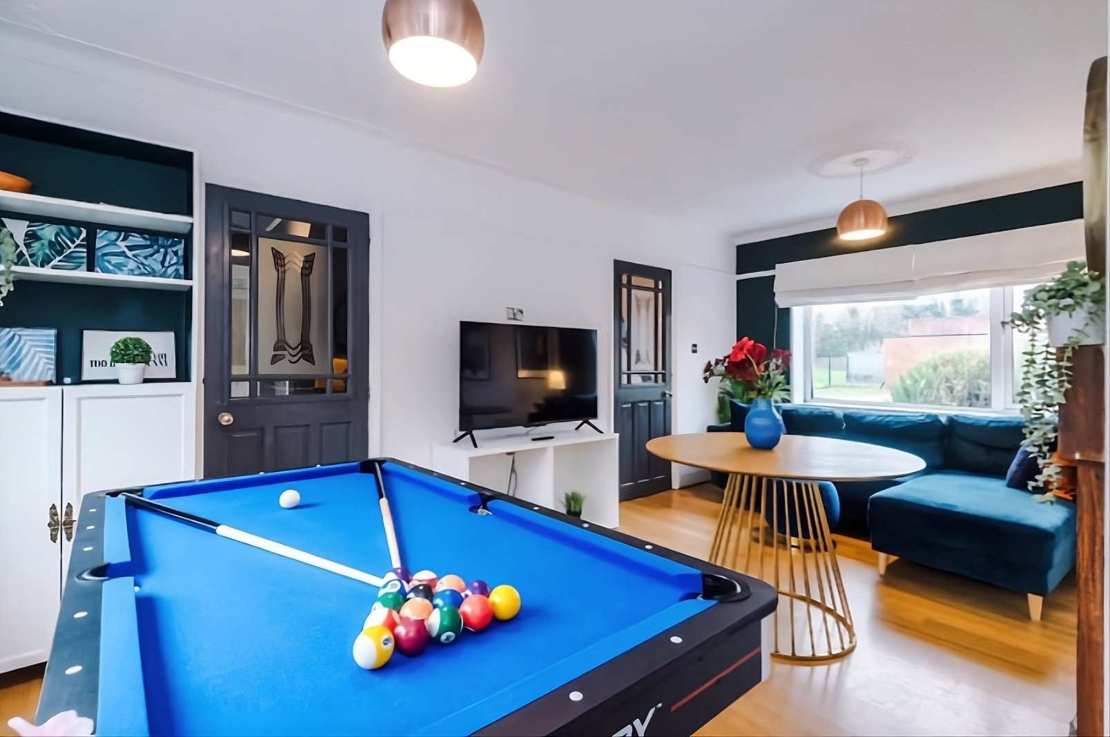Modern living and dining area with a blue pool and ping pong table, games console and 50" smart TV, also a large sofa bed.