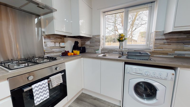 Modern kitchen with white cabinetry, gas stove, washing machine, and window overlooking garden