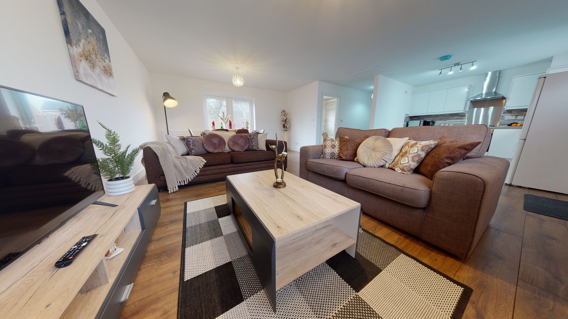 Bright open-plan living room with brown sofas, wooden coffee table and TV