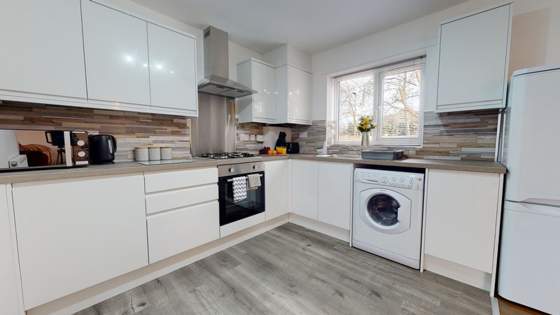 Modern white kitchen with stainless steel appliances, wood-effect flooring and bright windows