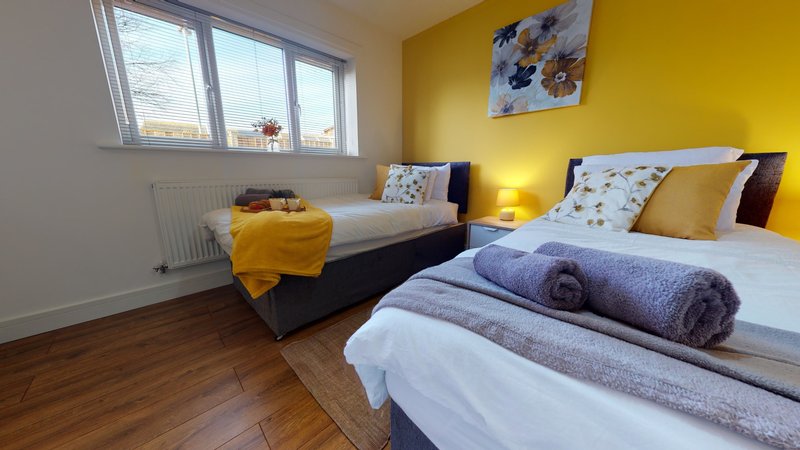 Bright yellow bedroom with two single beds, rolled towels, wooden floor and window