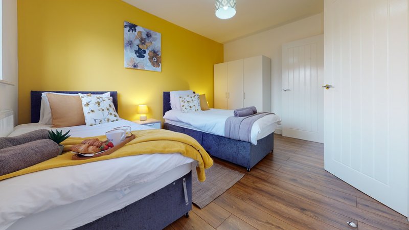Bright yellow bedroom with two beds, wooden flooring, bedside lamps and wall art