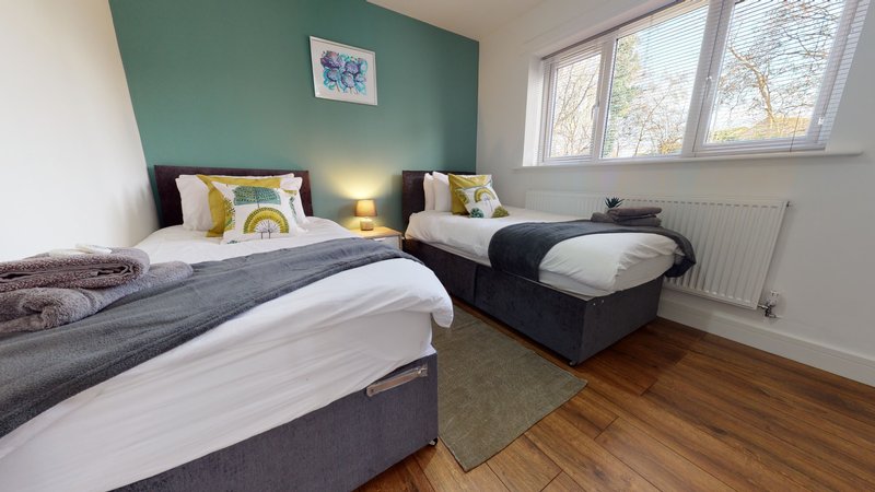 Bright bedroom with two single beds, green accent wall, wooden flooring and large windows