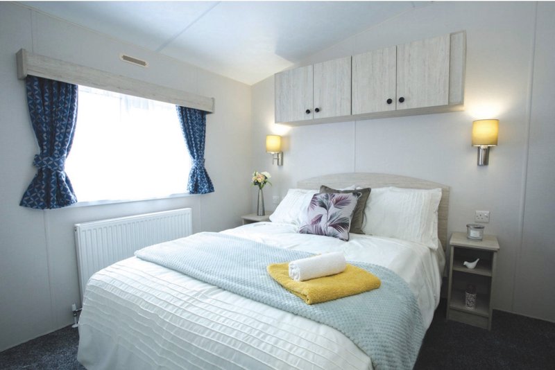 Bright bedroom with double bed, white bedding, yellow towel, blue curtains, wall sconces