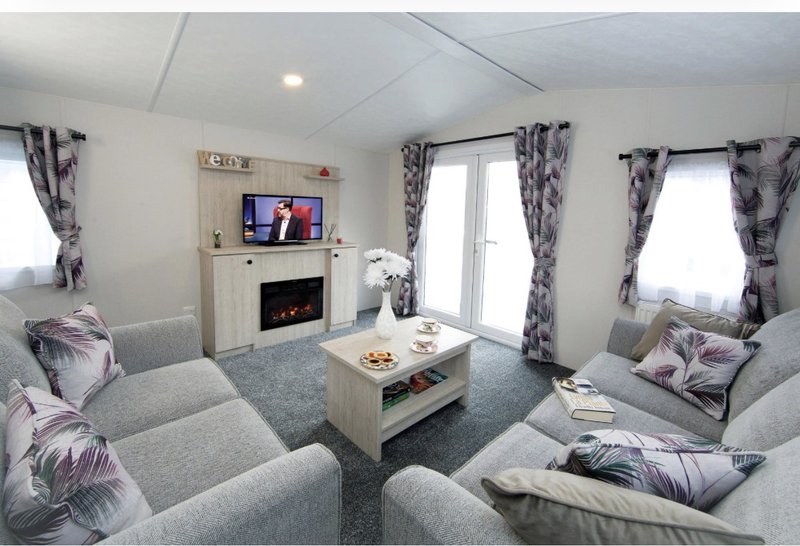 Modern living room with grey sofas, fireplace with TV, coffee table and patterned curtains