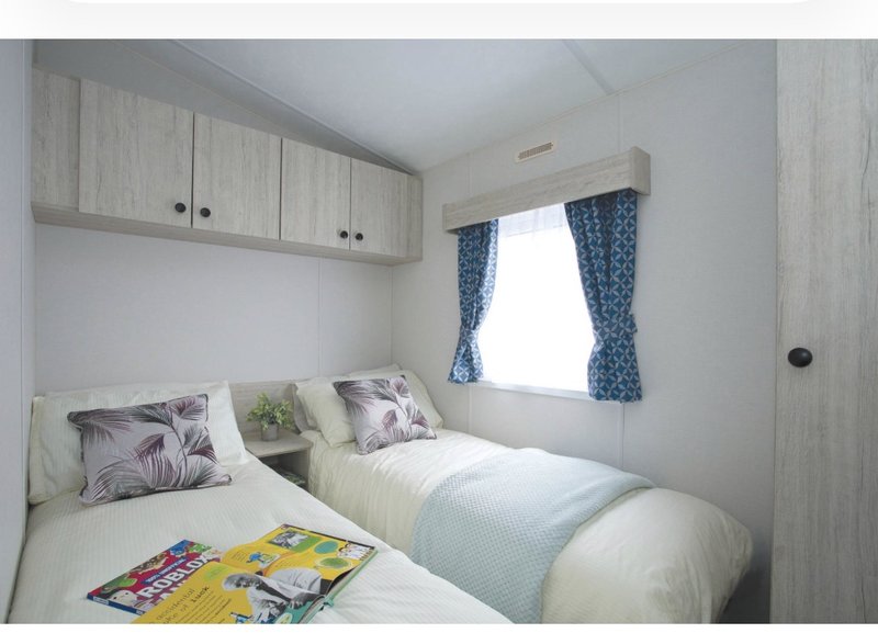 Twin bedroom with storage cupboards, decorated pillows, and window with blue curtains