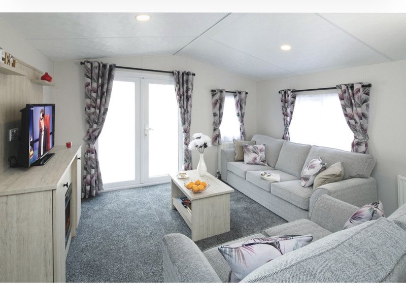 Modern living room with grey sofas, wooden coffee table, TV, patterned curtains and natural light
