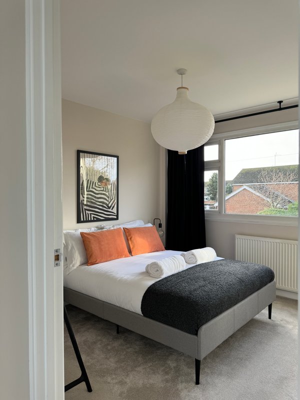 Modern bedroom with white bed, orange pillows, black pendant lamp and framed artwork