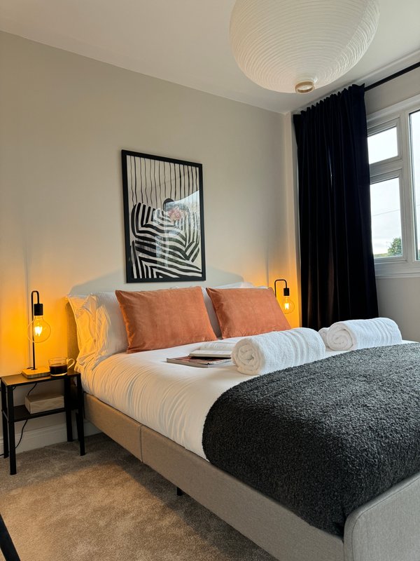 Modern bedroom with double bed, orange bedside lamps, black framed wall art, and dark curtains