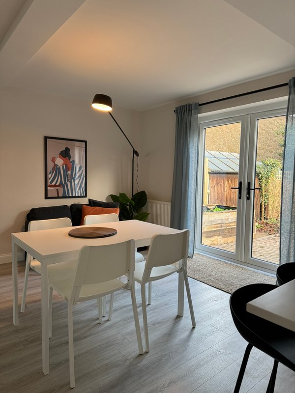 Bright dining area with white table, chairs, pendant lamp, and glass doors to garden