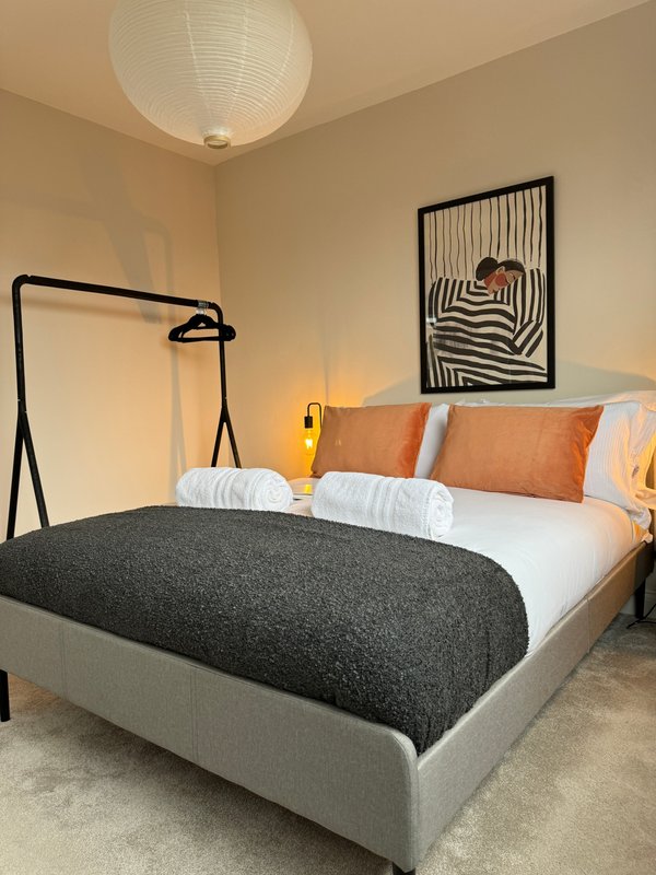 Modern bedroom with gray upholstered bed, white bedding, orange pillows, black pendant lamp and framed wall art.