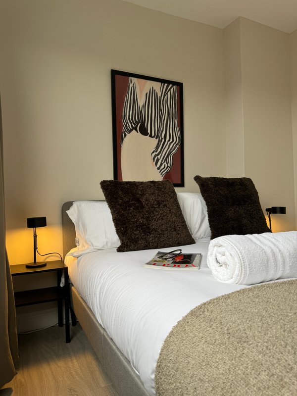 Modern bedroom with white bedding, dark cushions, framed wall art, and bedside lamps