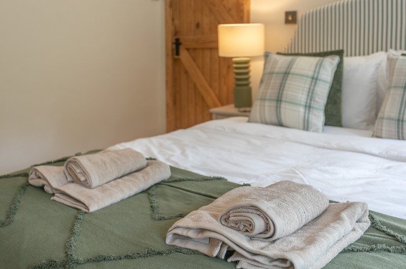 Bedroom with double bed, rolled towels, plaid pillows, wooden door and bedside lamp