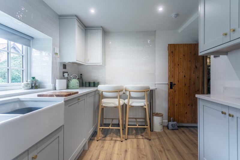 Modern galley kitchen with white cabinetry, wooden bar stools, sink and appliances