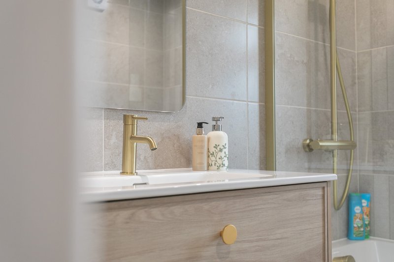Modern bathroom sink with gold faucet, mirror, and tiled wall backdrop