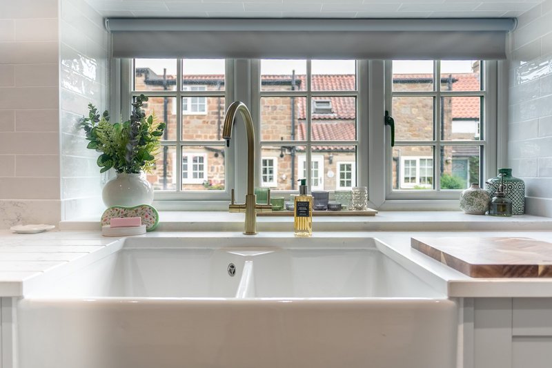 Modern white kitchen with farmhouse sink, large window overlooking street, potted plant and toiletries