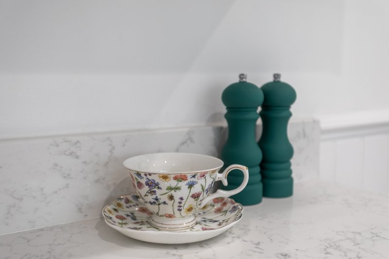 Marble countertop with decorative teacup, saucer, and green pepper mills