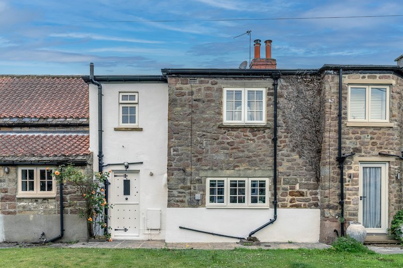 Stone and rendered cottage exterior with white-framed windows, green lawn and chimneys