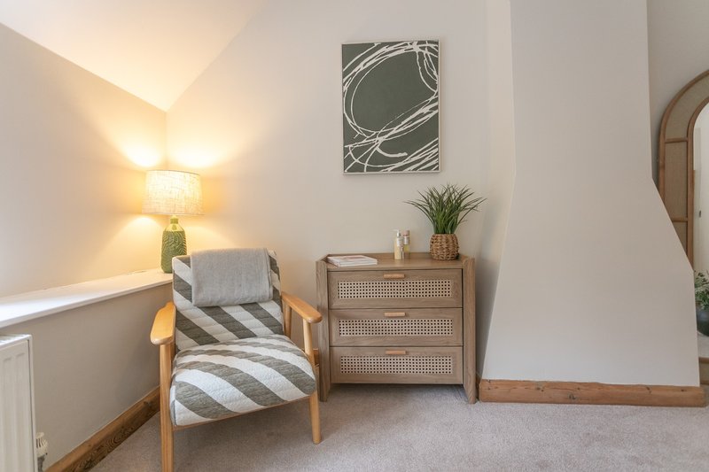 Bright bedroom corner with wooden armchair, striped cushions, rattan dresser and wall art