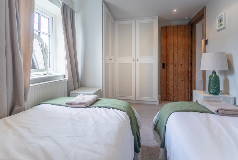 Twin bedroom with white beds, green throws, wooden door, wardrobe and window with curtains