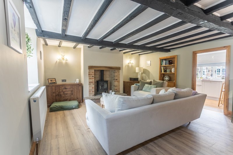 Open-plan living room with exposed beam ceiling, cream sofa, wood burner and wooden flooring