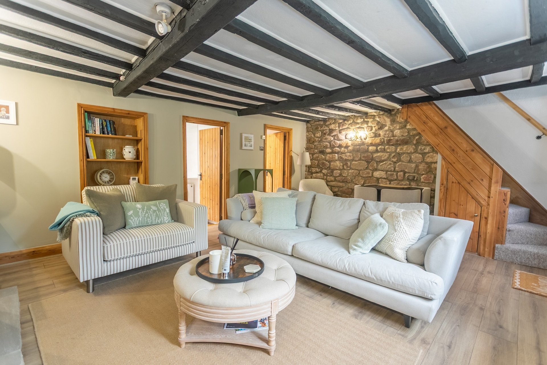 Open-plan living room with cream sofa, striped armchair, wooden beams and stone fireplace