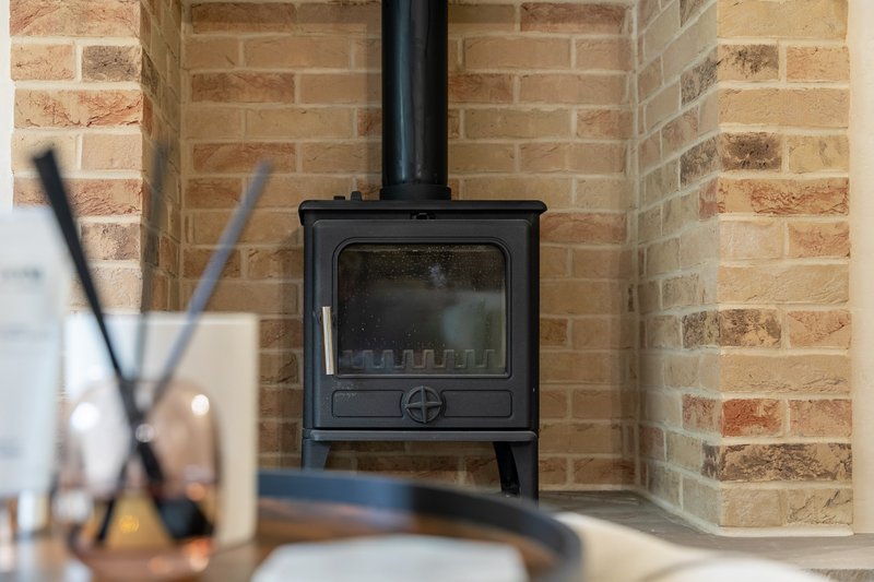 Black wood-burning stove mounted on brick wall with chimney pipe