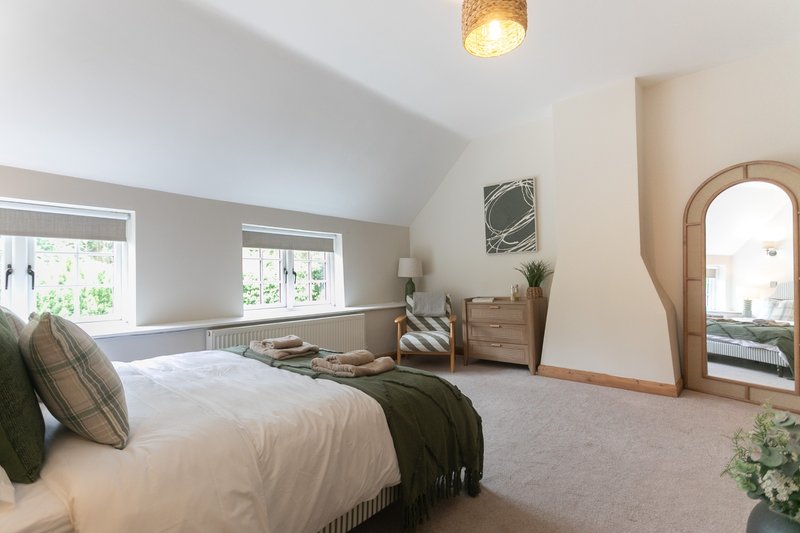 Spacious bedroom with double bed, wooden furniture, large mirror and windows