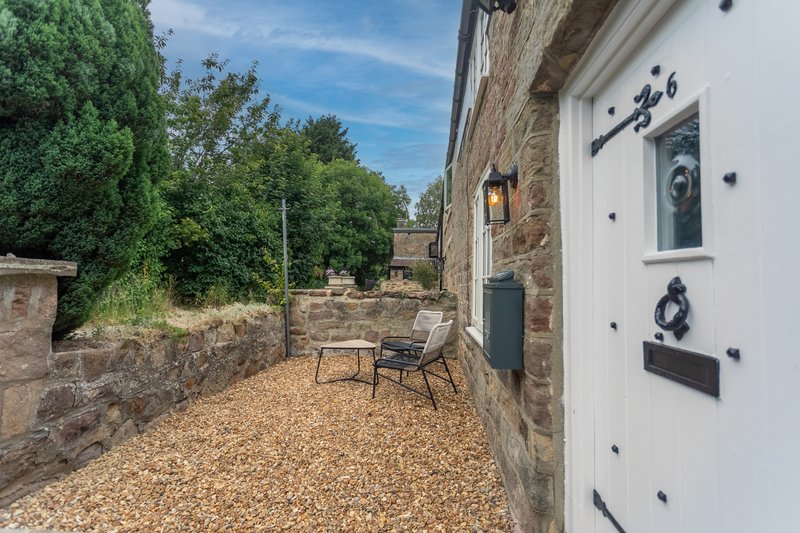 Stone cottage exterior with gravel patio, seating area, and garden views