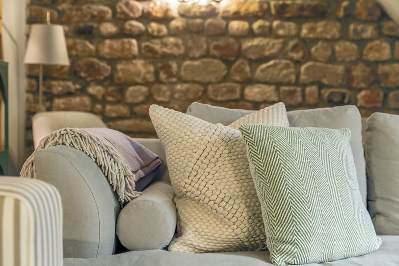 Neutral sofa with decorative cushions and throw against exposed stone wall