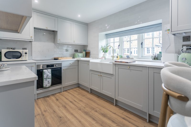 Modern kitchen with light gray cabinetry, white countertops, wooden flooring and large window