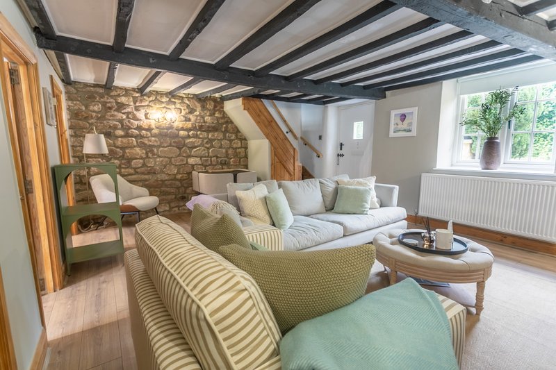Spacious open-plan living room with stone wall, exposed beams, comfortable seating and natural light