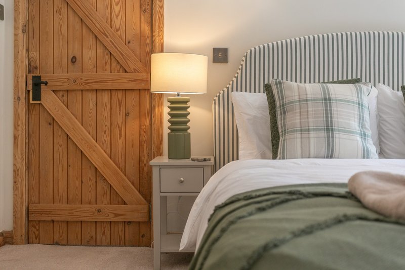 Bedroom with wooden barn door, bed with green and white bedding, striped headboard, and bedside lamp