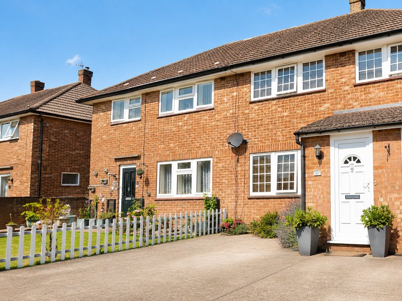 Brick semi-detached house with white picket fence, driveway and potted plants