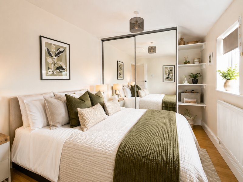 Bright bedroom with double bed, olive green bedding, mirrored wardrobe and built-in shelving