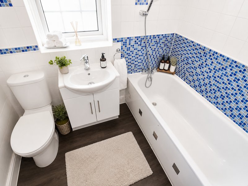 Modern bathroom with white toilet, sink vanity, blue tile feature wall and bathtub