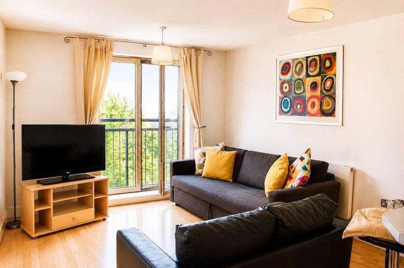 Modern living room with black sofa, TV, wooden floor, and balcony doors with golden curtains