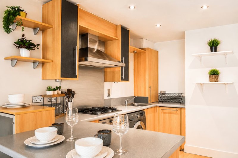 Modern kitchen with wooden cabinets, gas hob, island countertop and potted plants on shelves