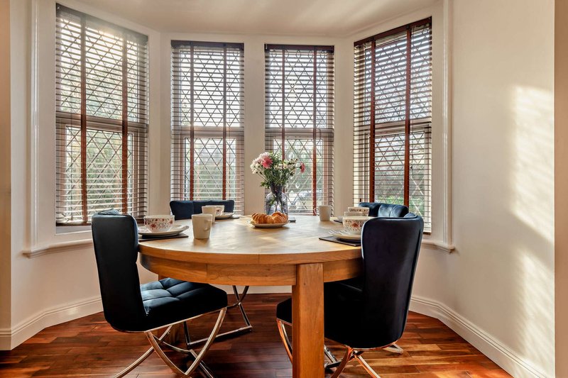 Dining room with round wooden table, black chairs, and large windows with shutters