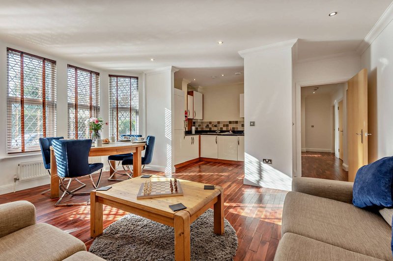 Open-plan living room with wooden furniture, blue chairs, sofa, and kitchen area visible