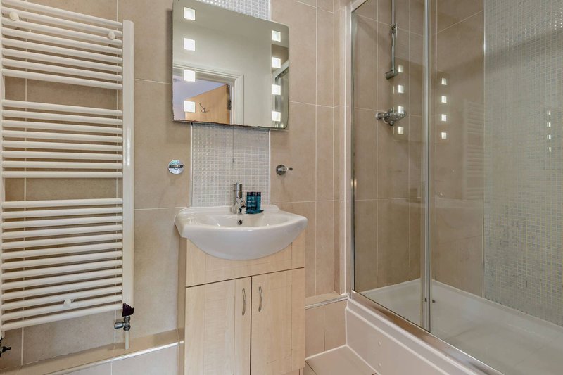 Modern bathroom with vanity sink, illuminated mirror, heated towel rail and shower enclosure