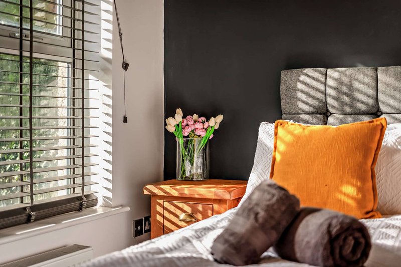 Bright bedroom with bed, orange cushion, flowers in vase, and shuttered windows