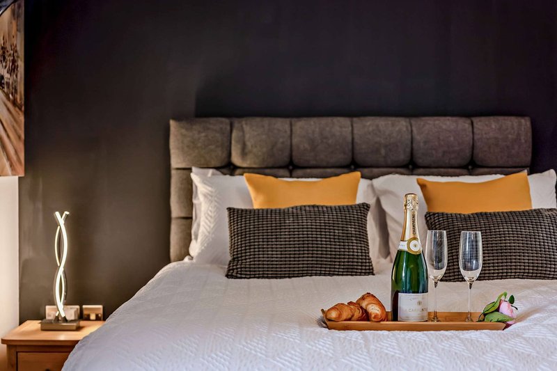 Modern bedroom with upholstered headboard, white bedding, yellow pillows, and champagne bottle on bed tray