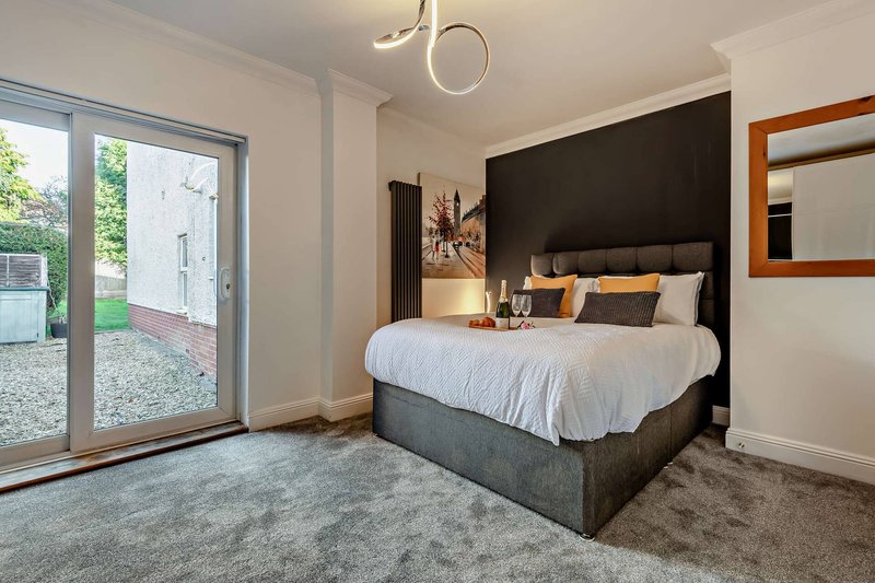Modern bedroom with king bed, black accent wall, pendant light and glass door to garden