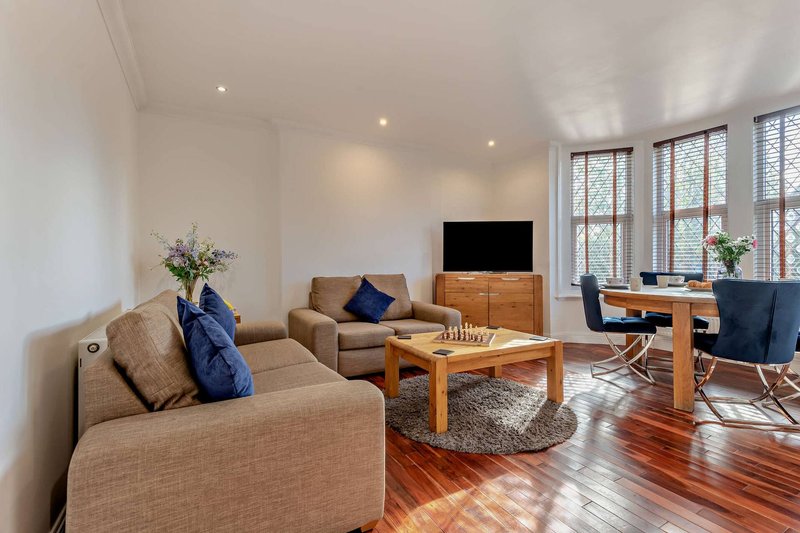 Spacious modern living room with beige sofas, wooden coffee table, wall-mounted TV, and hardwood flooring