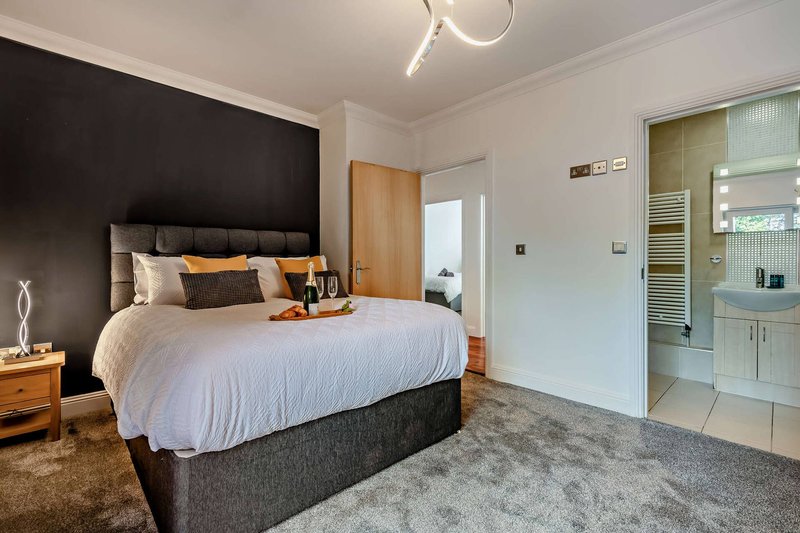 Modern bedroom with double bed, black headboard, orange accents and ensuite bathroom door