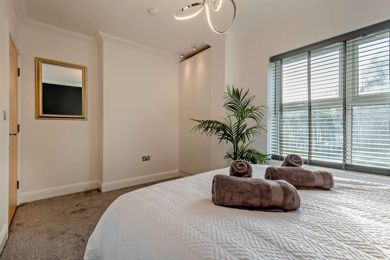 Modern bedroom with double bed, rolled towels, potted plant, and large windows with shutters