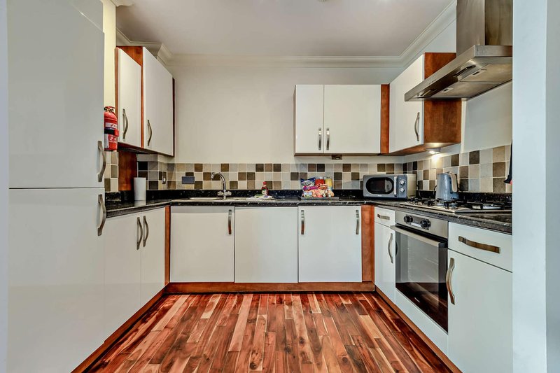 Modern kitchen with white cabinets, black countertop, checkered backtile and wooden floor