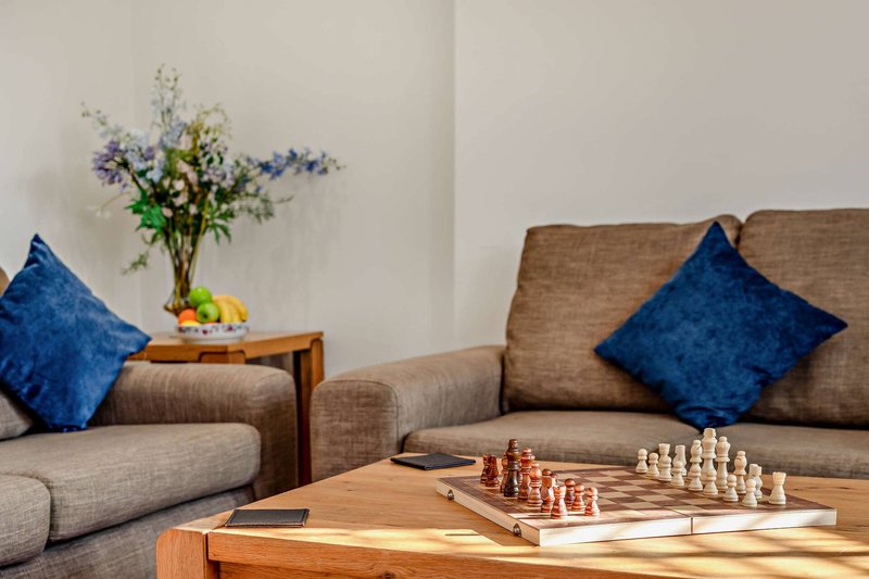 Living room with brown sofa, blue cushions, wooden coffee table with chess set, and fresh flowers in vase