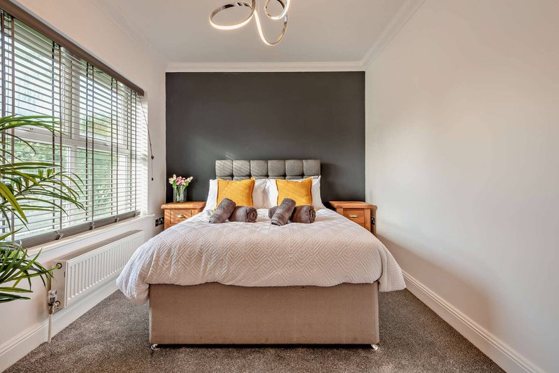 Modern bedroom with double bed, grey headboard, yellow pillows and potted plant by window